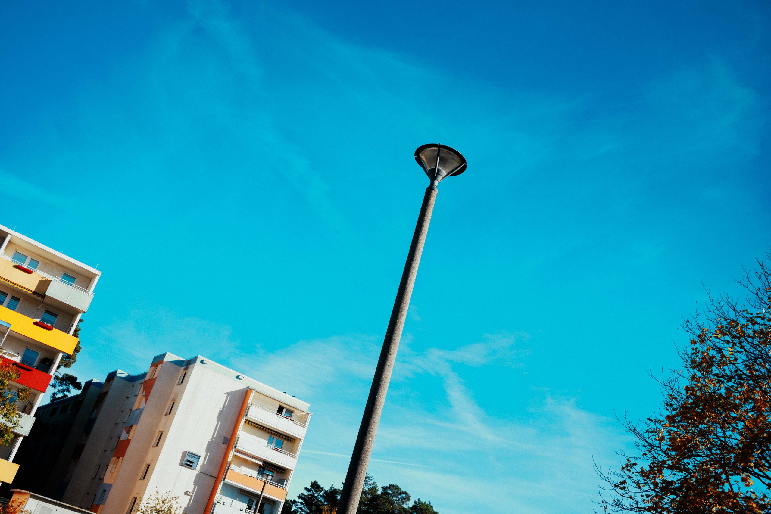 Eine Laterne vor einem blauen Himmel, weiter hinten ein Neubauhaus